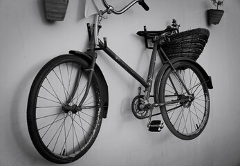 Naklejka na ściany i meble Black and white street photo with a bicycle hanging on the wall. The installation is an old rural bicycle with a large basket behind the seat hanging on the wall of a rural house.