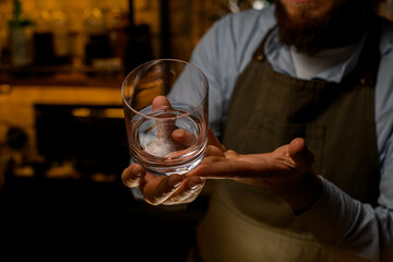 hands of a male bartender gently holding a transparent empty glass for booze