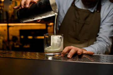 process of making a cocktail - pouring beverage from a shaker into a glass