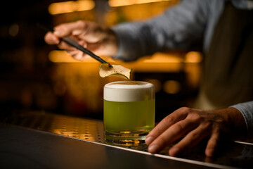 focus on slice of dry apple over a glass with a bright green foamy cocktail on the bar