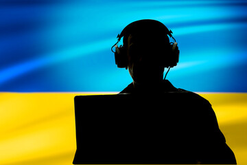 Silhouette of a military man in headphones with a laptop against the background of the flag of...