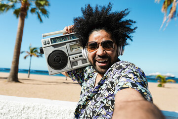 African American man listening music with vintage boombox stereo outdoor with beach in background -...