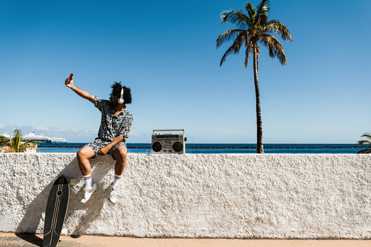 African man having fun doing selfie with beach on background - Focus on hand holding mobile phone
