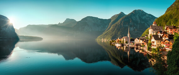 The iconic Austrian town Hallstatt in early morning light, a panoramic gorgeous landscape with the mountains, the houses and the teal sky reflected in the water of the lake