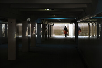An underground passage with a woman walking in front. Color and light composition with reflection on the surface of the walls in the underpass. Conceptual photography is a play of light, shadow and co