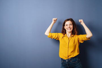 young celebrating business woman with raised arms against blue background