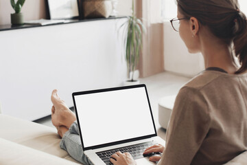 Young woman using laptop computer with white mockup screen at home. Freelance, student lifestyle, education, technology and online shopping concept.