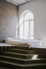 a bed on the podium in a room with white walls and large windows. minimalistic and bright interior...