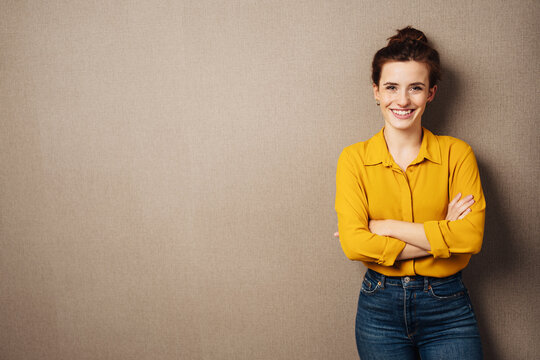 young smiling business woman with yellow blouse stands in front of brown background