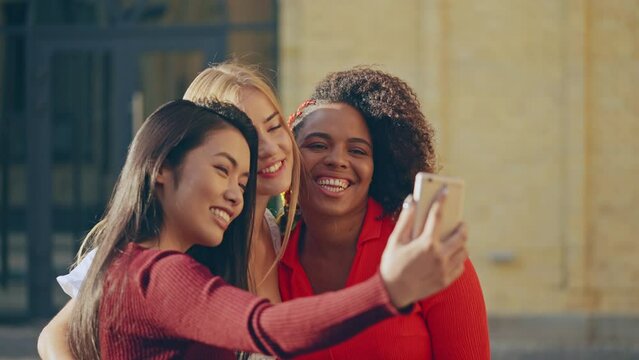 Happy multiethnic female friends grimacing and making selfie on smartphone