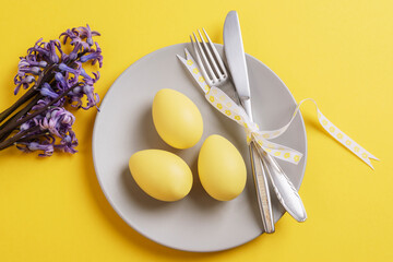 Gray plate with easter painted eggs on yellow background with hyacinth blue flowers. Happy Easter card. Top view, flat lay