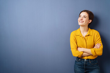 young business woman with yellow blouse stands in front of blue background and looks up laughing