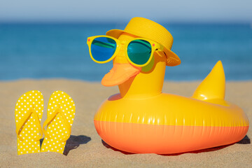 Beach flip-flops and yellow duck on the sand against blue sea and sky