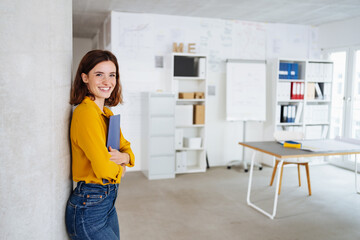 young smiling woman standing in office with cv in hand looking into camera