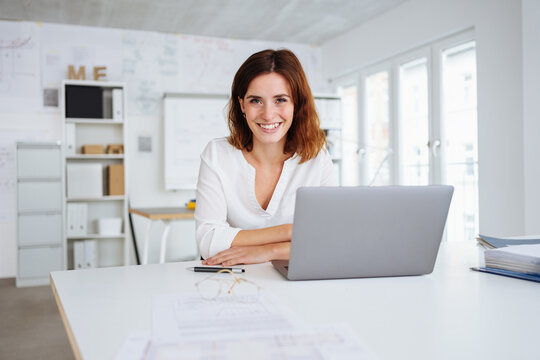 Young Laughing Woman Sits At Desk In Office And Looks Into Camera