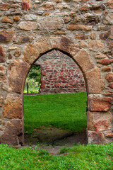 Passage through an old sandstone wall in the form of a pointed arch in a ruined monastery with deep green grass on the ground