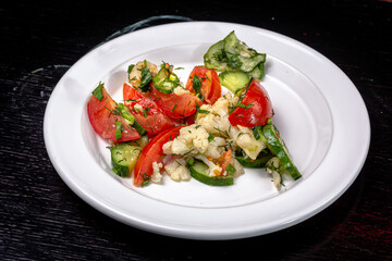 A simple vegetable salad of tomatoes, cucumbers and cauliflower, seasoned with olive oil lies on a white plate
