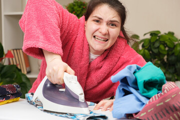 A housewife in a pink robe is hard to iron clothes with a bad iron, angry and nervous. Fatigue from...