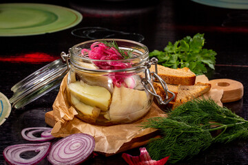 Herring or smoked mackerel with potatoes and onions are in a glass jar.