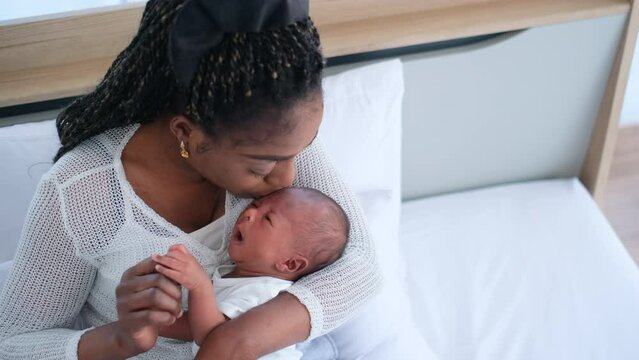 African American mother hold newborn baby on her chest and kiss head of baby stay in bedroom of their house.