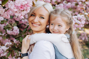 Close up of daughter hugging mom sitting on her back on cherry sakura background. Walk in the...