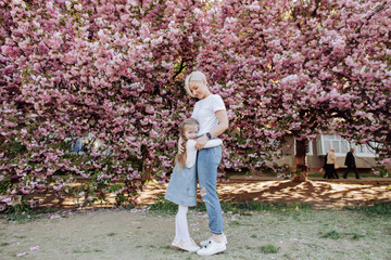 Young mother with her child have fun in the park near the sakura. Family (mother and children) in spring city street with pink japanese cherry trees blossom (Uzhhorod City, Ukraine). Sakura blossomed.