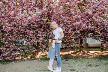 Young mother with her child have fun in the park near the sakura. Family (mother and children) in spring city street with pink japanese cherry trees blossom (Uzhhorod City, Ukraine). Sakura blossomed.