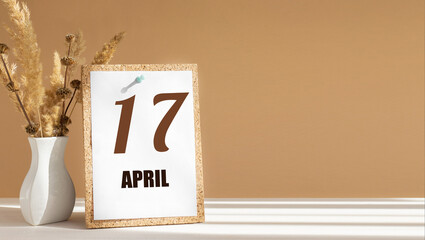 April 17. 17th day of month, calendar date.White vase with dead wood next to cork board with...