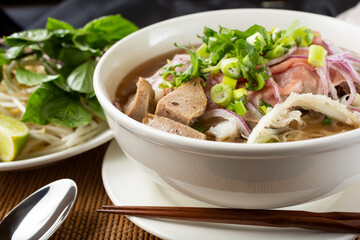 A view of a large bowl of pho with a variety of meat inside, in a restaurant or kitchen setting.