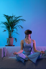Woman is engaged in meditation sitting home on couch. Yoga with virtual glasses. Lifestyle...