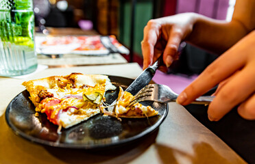 Fototapeta na wymiar woman hands with knife and fork cutting pizza on table in cafe