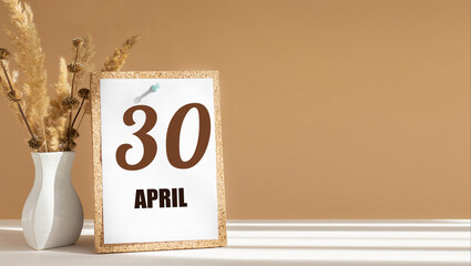 April 30. 30th day of month, calendar date.White vase with dead wood next to cork board with numbers. White-beige background with striped shadow. Concept of day of year, time planner, spring month