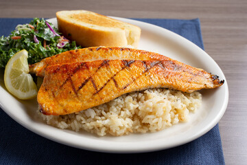 A view of a trout fillet over rice, on a plate with a Texas toast slice and kale salad.