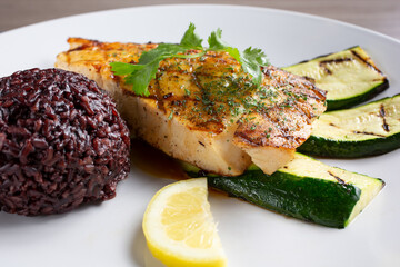 A view of a halibut fillet, with a side of black rice and grilled zucchini.