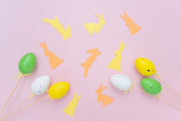 Top view photo of easter decorations easter bunnies yellow and beige and easter eggs on isolated pastel pink background with copyspace. Easter composition for the cover.