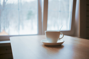 A cup on the table in front of the window.