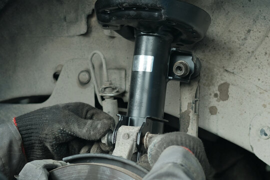 Car maintenance at the service center. Replacement of the front strut of the shock absorber. The mechanic fixes the position of the shock absorber strut with a mounting bolt.