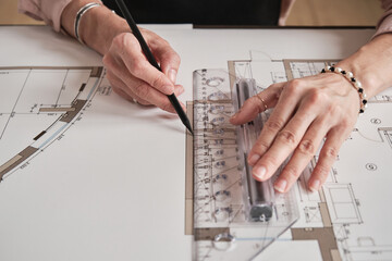 Close-up of unrecognizable design architect in bracelets using transparent ruler while working with floor plan