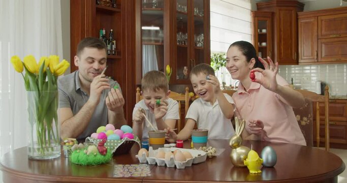 family of 4 members smile, paint eggs and show in what colors they painted eggs