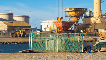 Zone industrielle portuaire, à Port-La-Nouvelle.  De nombreux engins de chantier circulent, tandis que d'immenses grues sont régulièrement actionnées pour transporter des containers