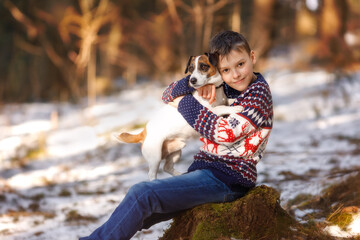 Boy with dog Jack Russell Terrier in the forest at sunset. Two huging best friends portrait - kid and dog sitting on the tree stump