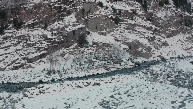 Aerial view of a river flowing in between the mountains covered with snow 