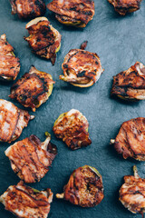 Fig halves in grilled bacon on black plate, view from above. Food catering buffet.