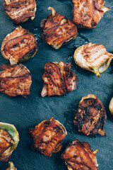 Fig halves wrapped in grilled bacon on black plate. Food catering buffet.