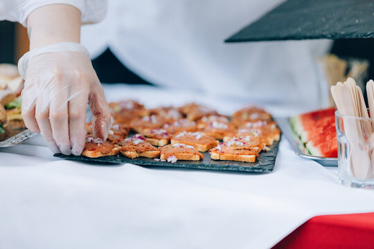 Human hand wearing a hygienic glove arranging toasts with beafsteak tatar. Food catering buffet.