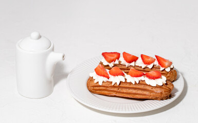 Eclairs with cream and strawberries on a white plate. 