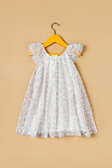 White baby dress with flowers on a hanger on a beige background. Fashion kids outfit for summer.