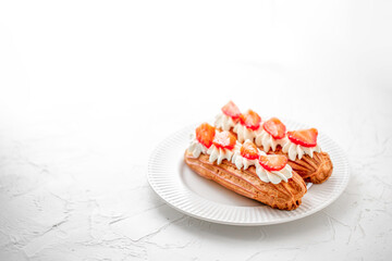 Eclairs with cream and strawberries on a white plate. 