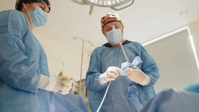 Laparoscopic instrument. Close up of female hands in sterile gloves giving trocar for laparoscopy procedure to doctor. The surgeon's doing laparoscopic surgery in the operating room. Minimally surgery