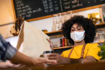 African Woman barista  wear mask due to Covid-19 pandemic, receive drink on coffee bar counter. Restaurant worker giving takeaway delivery food bag.Small business social distance concept.
